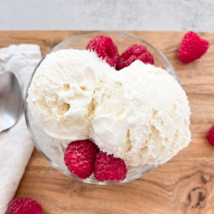 Creamy vanilla ice cream with fresh raspberries in a glass bowl on a wooden surface, perfect for a sweet summer treat.