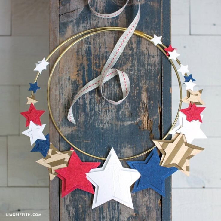 Patriotic star garland for July 4th or Memorial Day celebrations, featuring red, white, blue, and natural paper stars on a gold hoop with a red and white ribbon.
