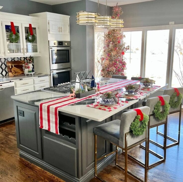Festive Christmas kitchen with a decorated island, holiday table setting, and a pink Christmas tree in a bright, modern space filled with natural sunlight.