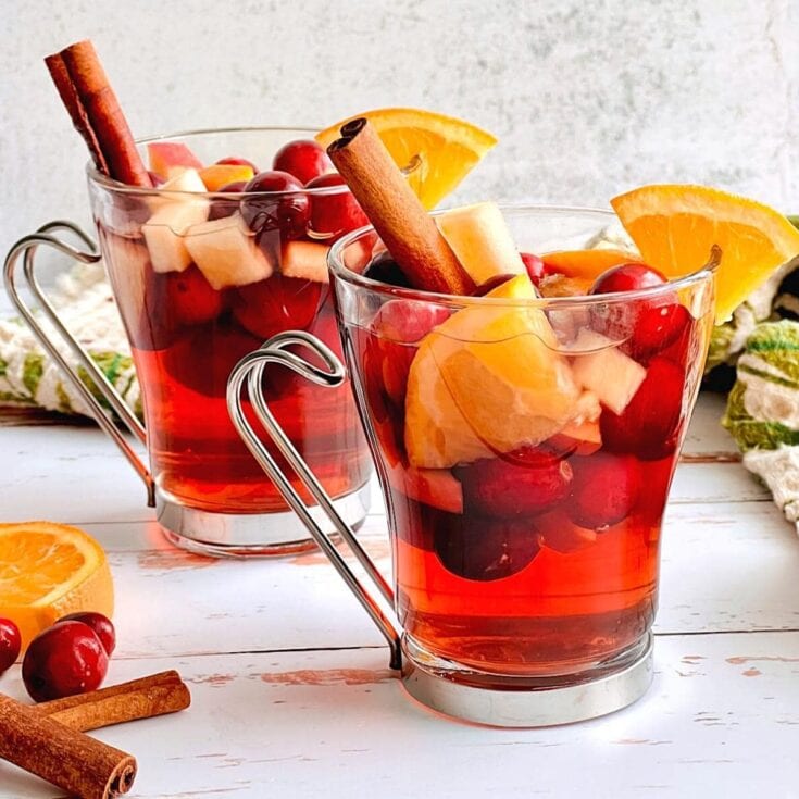 Sweet holiday sangria with fresh fruit slices, cherries, and cinnamon sticks in glass mugs - festive beverage perfect for gatherings and special occasions.