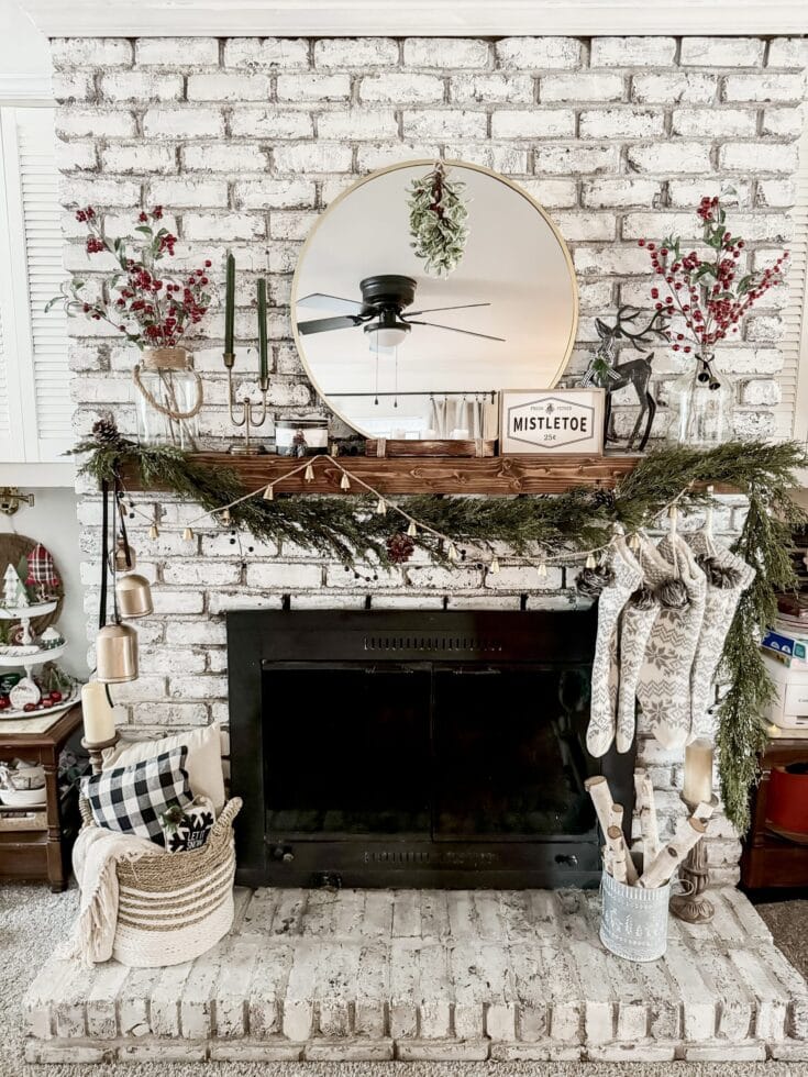 Rustic farmhouse Christmas fireplace decor with greenery, stockings, candles, and festive accessories, creating a cozy holiday atmosphere.