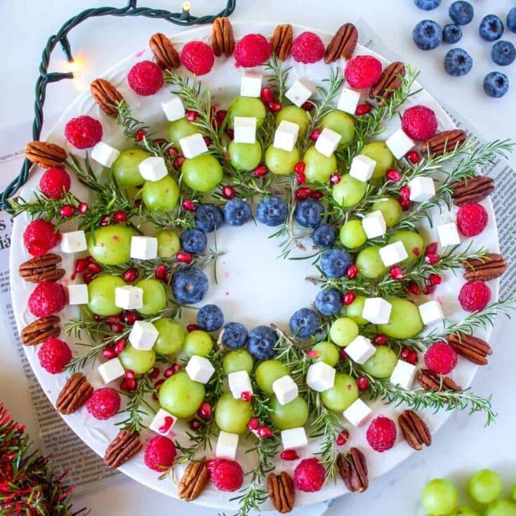 Fresh holiday fruit platter with grapes, blueberries, pomegranate, and herbs, garnished with marshmallows and pecans, perfect for festive gatherings.