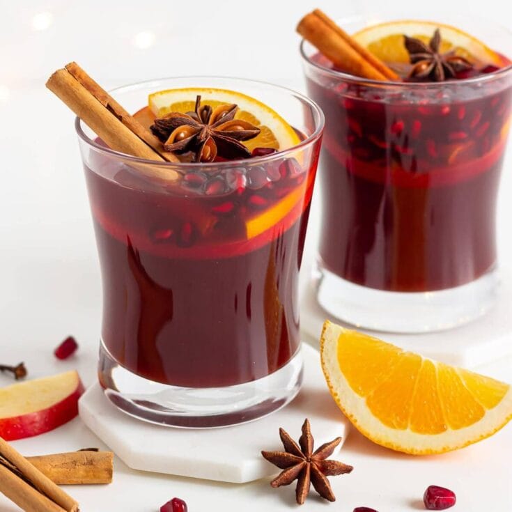 Mulled wine in two glasses garnished with orange slices, cinnamon sticks, and star anise, surrounded by fresh fruit and spices, perfect for cozy winter gatherings.