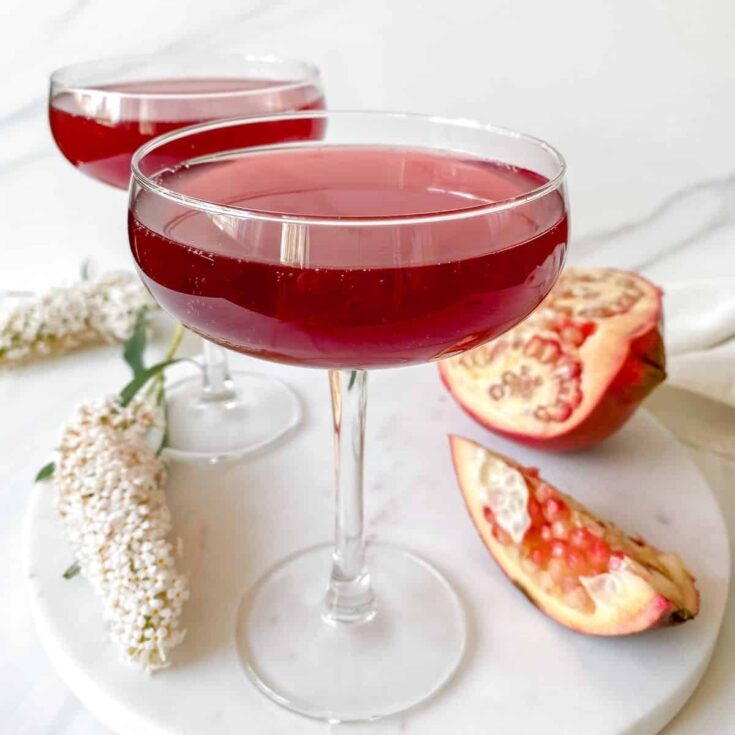 Sweet pomegranate wine in elegant coupe glasses, garnished with fresh pomegranate halves and white flowers, ideal for romantic occasions or special celebrations.