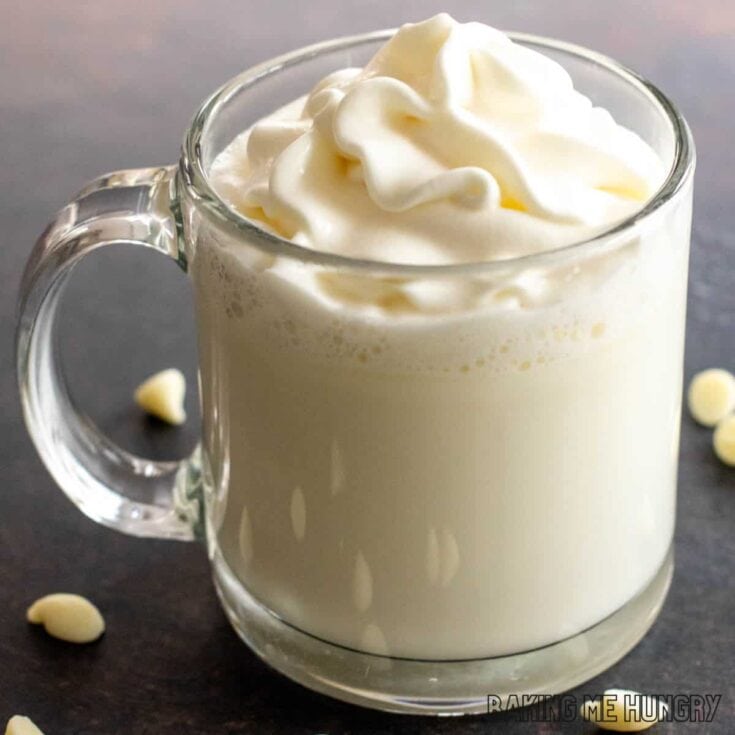Creamy white hot cocoa topped with whipped cream in a clear glass mug, perfect for cozy winter evenings and holiday celebrations.