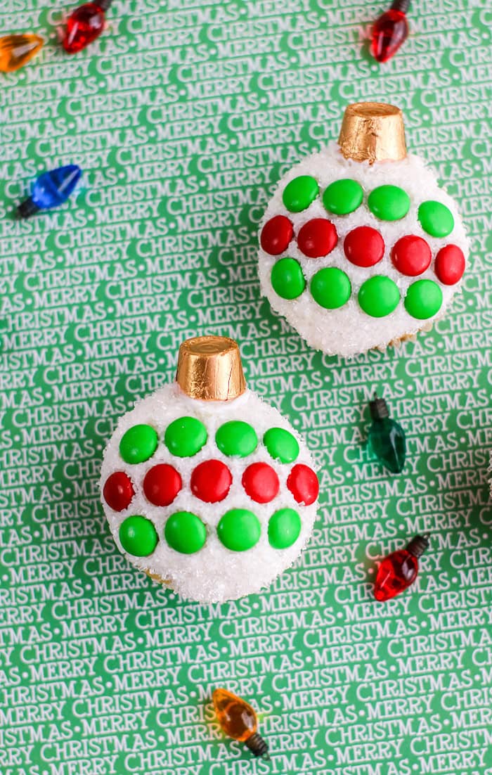Decorative Christmas cupcake with green and red candies on a snowy top, golden cupcake liner, and holiday-themed background with "Merry Christmas" text.