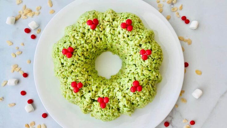 Festive green rice Krispie treat wreath decorated with red candy berries on a white plate, perfect for holiday desserts and Christmas celebrations.