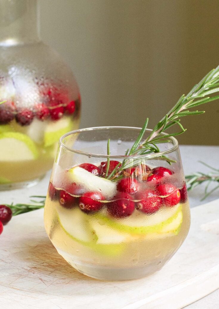 Fresh cranberry and citrus infused water with rosemary garnish in a clear glass, emphasizing healthy, festive beverage options with natural ingredients.