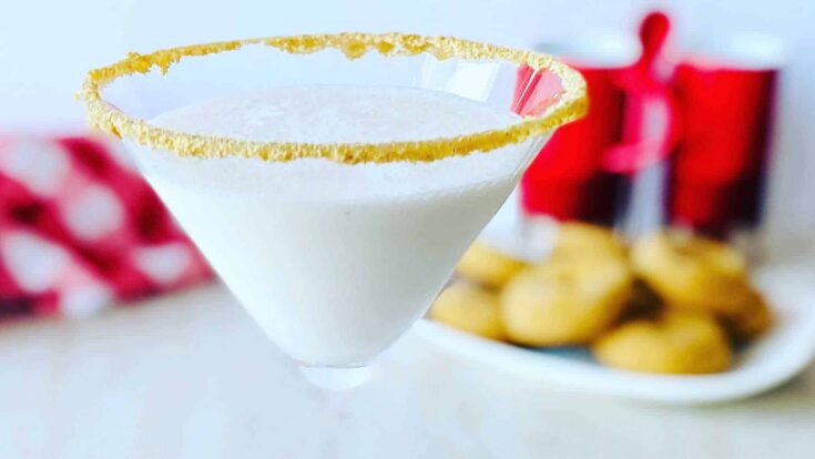 Creamy white cocktail in a martini glass with a salted rim, garnished with red and white polka dot napkin and a plate of cookies in the background. Perfect for Valentine’s Day or romantic celebrations.