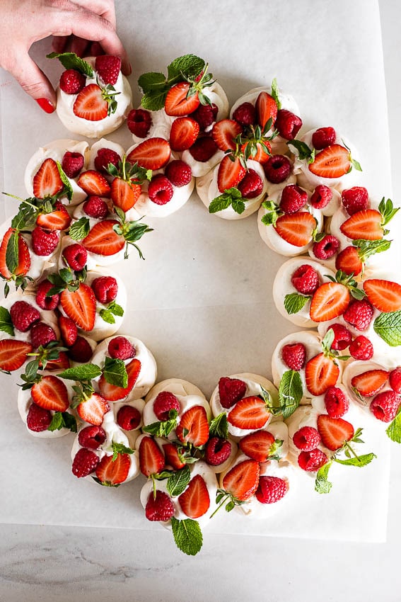 Fresh fruit pavlova wreath topped with strawberries, raspberries, and mint leaves for a colorful and delicious dessert. Perfect for celebrations, featuring whipped meringue base and vibrant berries.