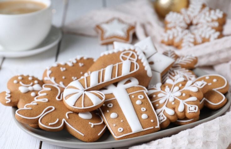 Decorative gingerbread cookies with white icing, holiday-themed shapes including stars and snowflakes, on a white platter for Christmas celebrations.