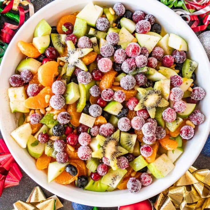 Fresh fruit salad with mixed berries, kiwi, pineapple, mandarin oranges, and chopped apples, garnished with sugared berries and pine nuts, perfect for holiday gatherings and celebrations.