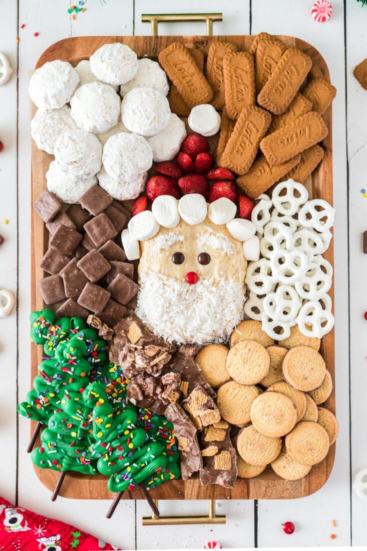 Colorful holiday charcuterie board with Santa face, cookies, strawberries, pretzels, chocolates, marshmallows, and candy canes, perfect for Christmas parties and festive treats.