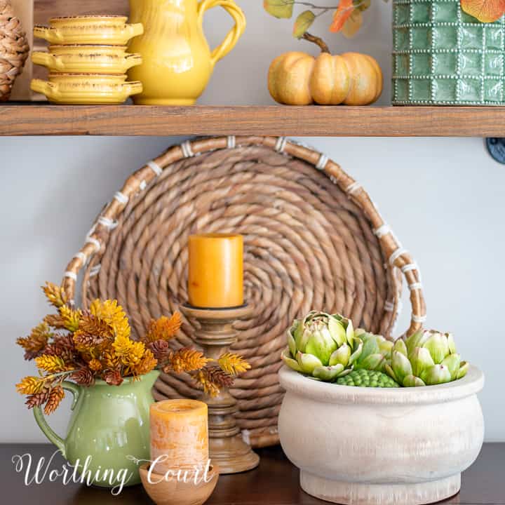 Pumpkin and fall decor arrangement with greenery, candle, and woven basket, perfect for autumn mantel or table centerpiece.