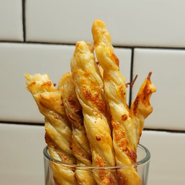 Golden cheesy twisted breadsticks served in a clear glass, crispy and appetizing, perfect for snack or appetizer.