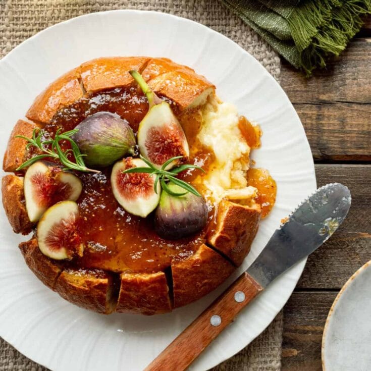 Delicious fig and mascarpone tart topped with fresh figs and herbs on a white plate, served with a knife on a rustic wooden table, perfect for dessert or brunch.