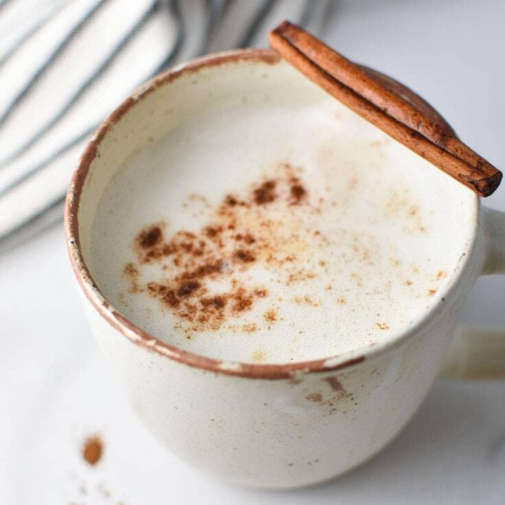 Creamy vanilla latte topped with cinnamon, served in rustic ceramic mug with a cinnamon stick garnish. Perfect cozy beverage for autumn or winter mornings.