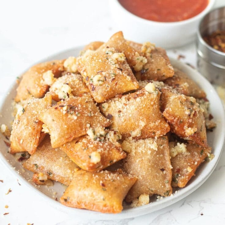 Golden fried pastries topped with crushed nuts and sugar, served on a white plate with side sauces, perfect for a sweet snack or dessert.