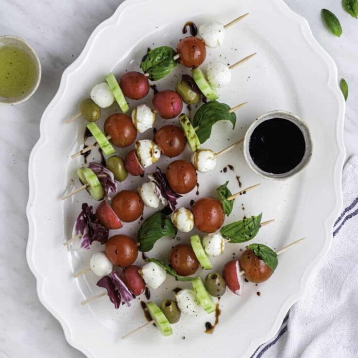 Fresh Caprese Skewers with Cherry Tomatoes, Mozzarella, Basil, and Balsamic Drizzle on White Serving Platter.