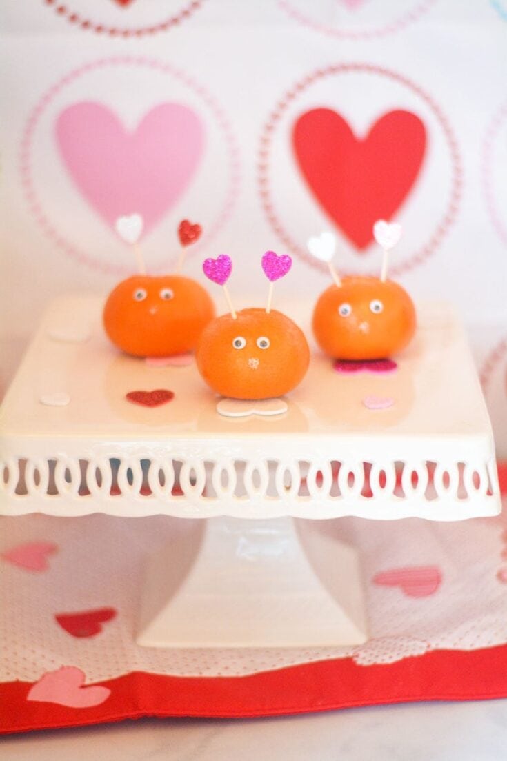 Colorful heart-themed cupcake toppers with adorable sweet faces, decorated on a white cake for Valentine's Day or romantic celebrations.