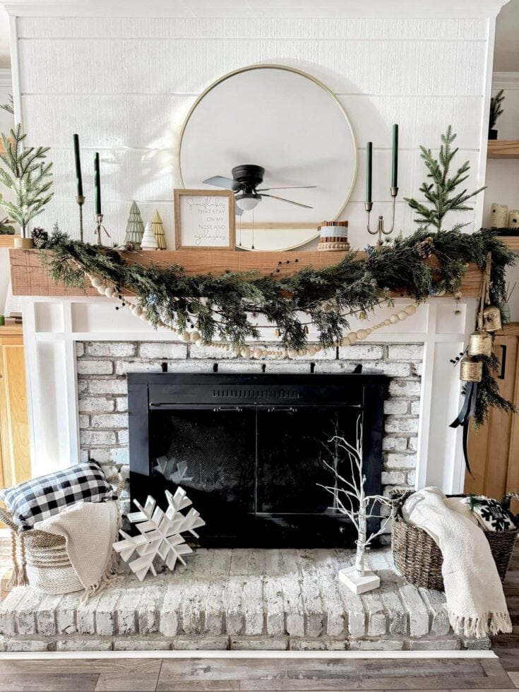 Rustic holiday decor over white brick fireplace with greenery garland, candles, and seasonal accents, creating a cozy and festive Christmas mantle display.