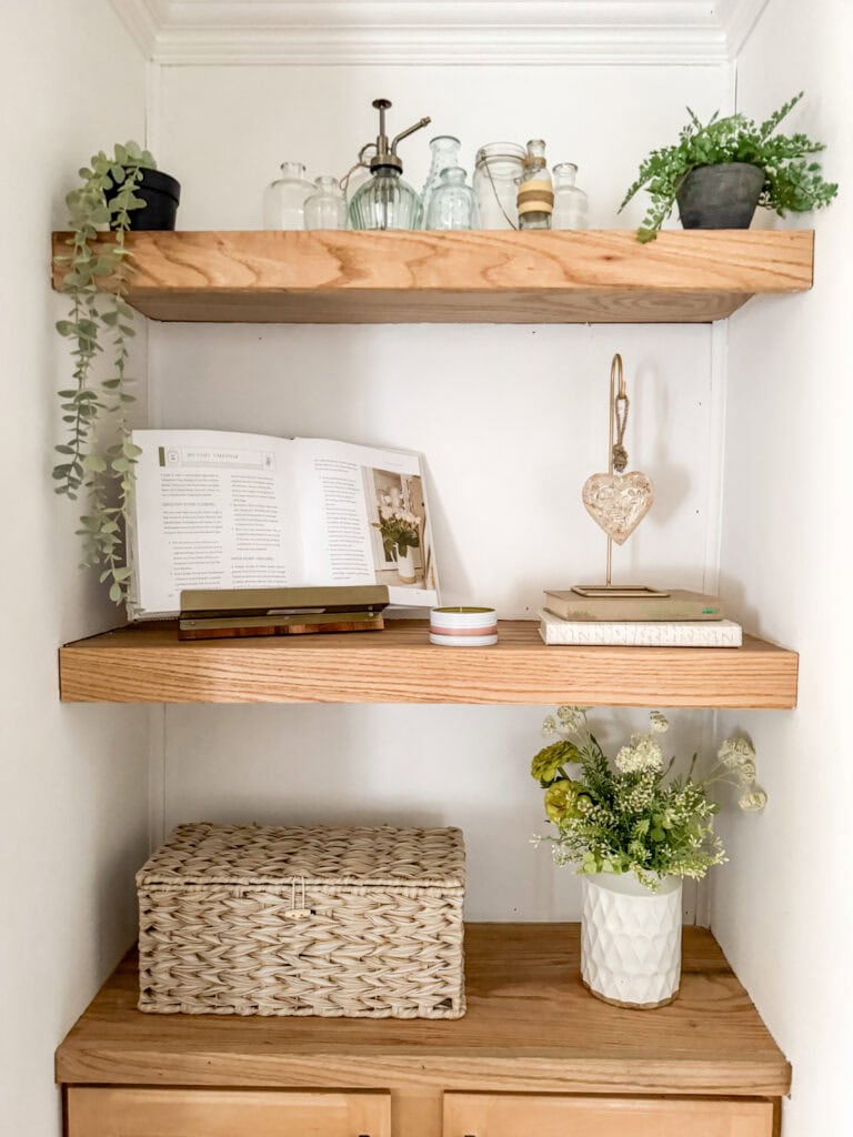 shelves with wood heart on stand, woven basket, bottles and glass jars, greens