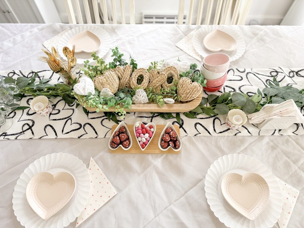 Fancy valentine's day table setting with heart-shaped plates, candies, and floral decorations for romantic celebration.