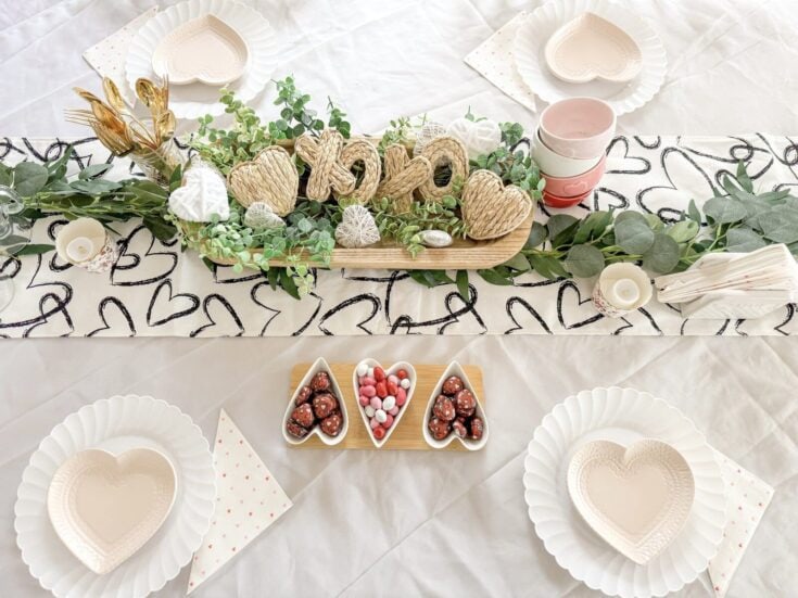 Rustic Valentine's Day table setting with heart-shaped plates, decorative greenery, and love-themed treats, creating a romantic and cozy atmosphere.
