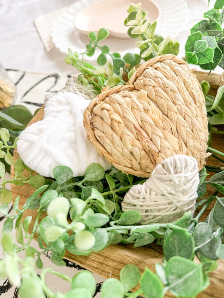 Soft woven heart, plush white towel, and natural greenery on a wooden tray, perfect for a cozy or romantic gift set.