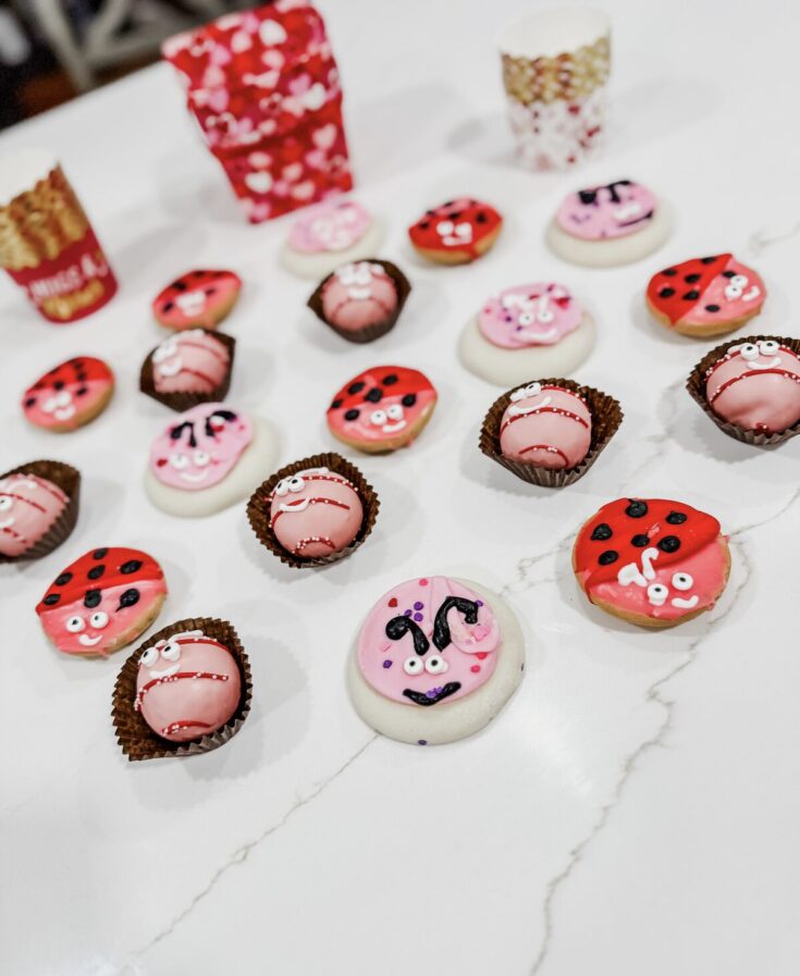 Colorful Valentine's Day cookies decorated with ladybug and adorable face designs, arranged on a white marble surface for a sweet celebration.