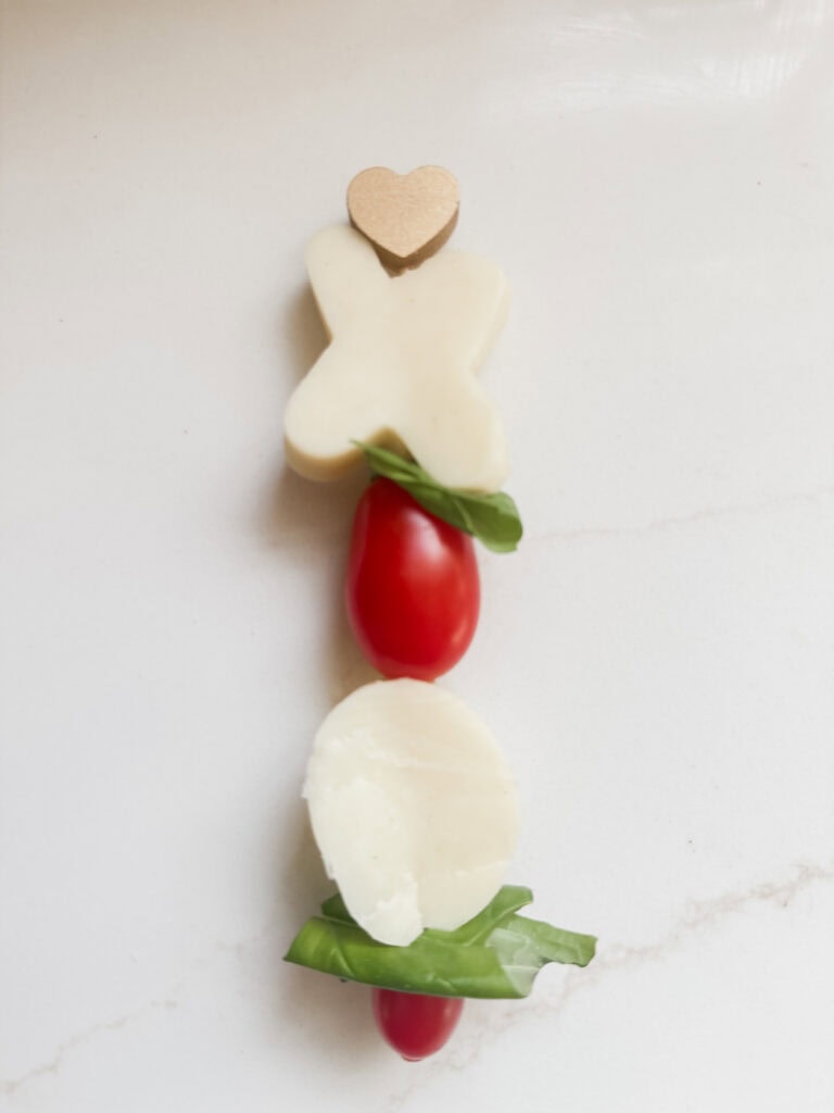 Delicious appetizer platter featuring cherry tomatoes, fresh basil, cheese slices, and a heart-shaped cheese piece, perfect for romantic gatherings or elegant events.