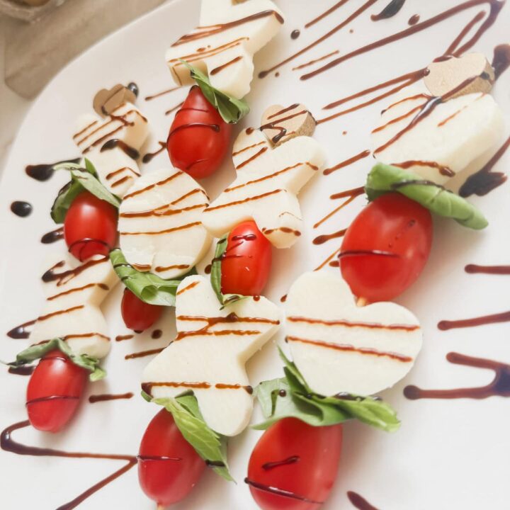 Sweetheart Caprese skewers with cherry tomatoes, mozzarella hearts, fresh basil, and drizzled balsamic glaze and chocolate, perfect for romantic occasions and Valentine's Day celebrations.