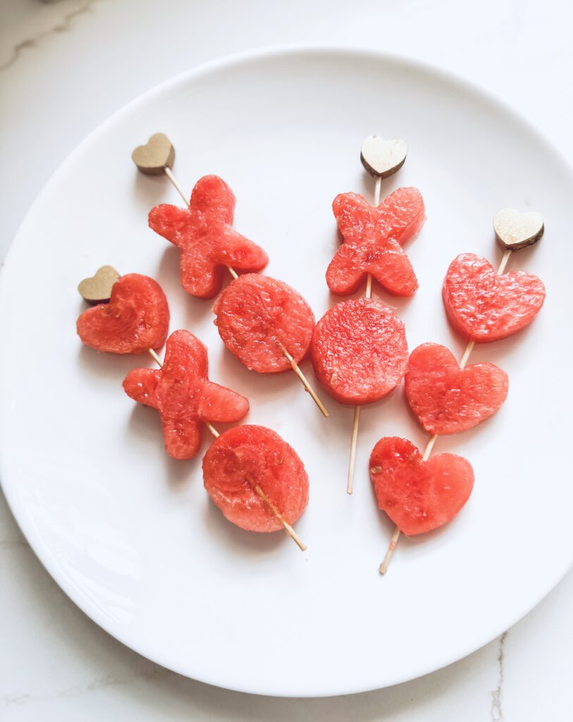 Juicy watermelon heart and bear-shaped slices on wooden picks, perfect for romantic or summer desserts. Fresh, vibrant, sweet watermelon treats on a white plate.