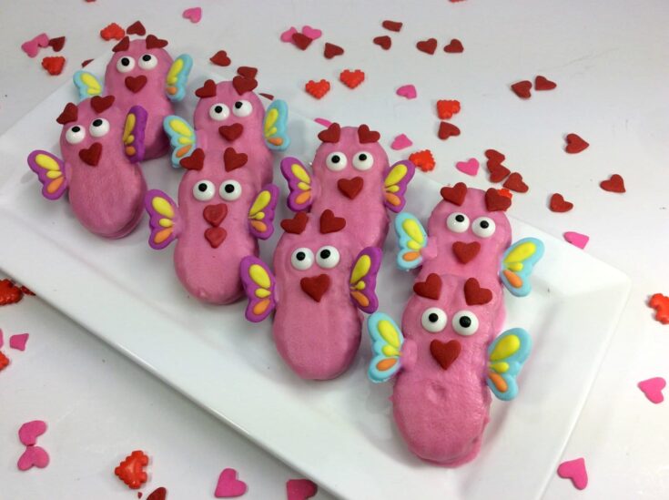 Colorful love bug cookies decorated with heart and butterfly details, perfect for Valentine's Day, birthdays, or special occasions, displayed on a white platter with heart-shaped sprinkles.