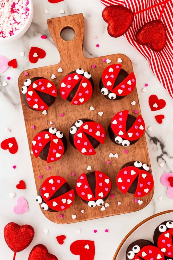 Red ladybug cupcakes with fondant hearts and googly eyes on a wooden board, perfect for Valentine's Day desserts and romantic celebrations.