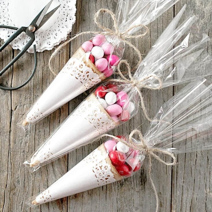 Colorful candy cones filled with pink, red, and white chocolates wrapped in clear plastic with rustic twine bows, perfect for Valentine's Day or special celebrations.