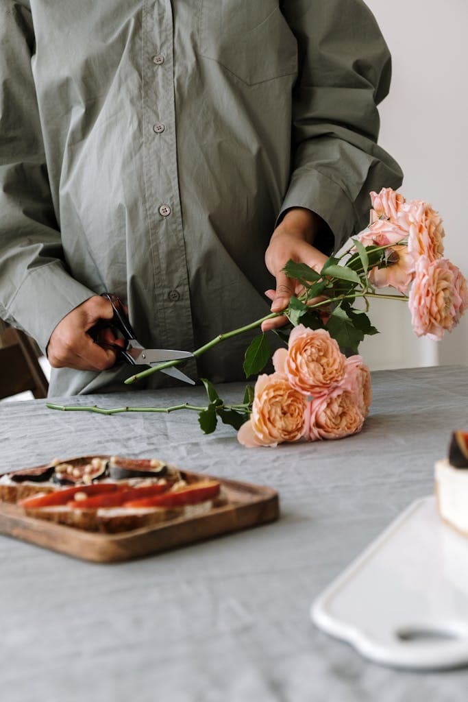 A person arranges peach roses beside a wooden board of bread and fruit slices.