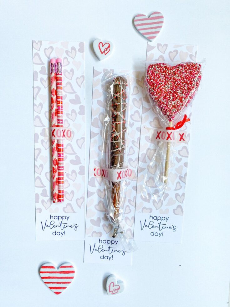 Delicious Valentine's Day treats including pink striped pens, a chocolate churro, and a heart-shaped lollipop with pink, white, and red sprinkles, all wrapped with love-themed labels and decorative hearts.