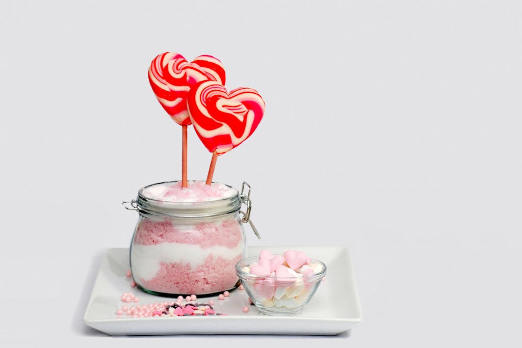 Heart-shaped lollipops and candy in a glass jar on a white plate, perfect for a sweet treat.
