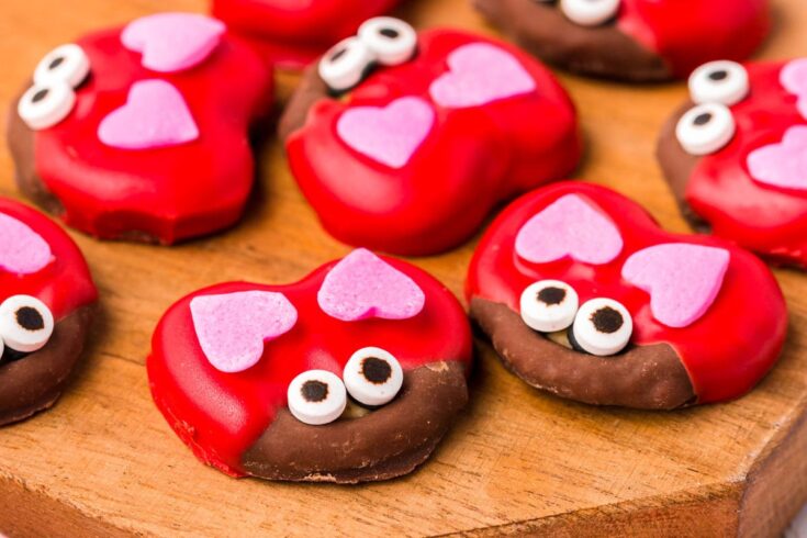 Colorful heart-shaped Valentine's Day cookies with pink heart toppings and candy eyes on a wooden board, perfect for romance and sweet treats.