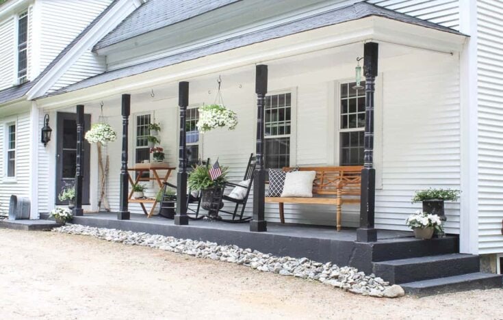 Cozy white farmhouse porch with black accents, hanging flower baskets, and wooden benches showcasing charming outdoor decor and comfortable seating for relaxation and outdoor gatherings.
