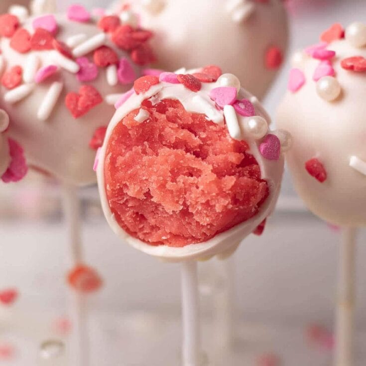 Pink cake pop with white chocolate coating and heart-shaped sprinkles, close-up.