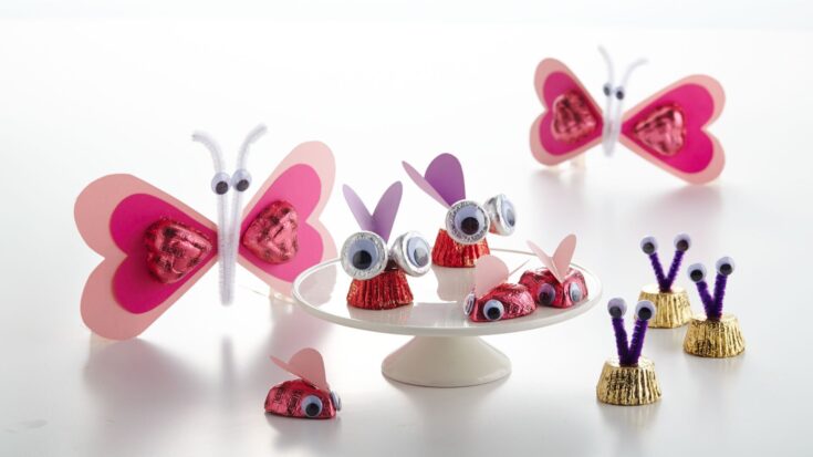 Colorful butterfly and bug-themed Valentine’s Day treat decorations made with Hershey's chocolates, googly eyes, pipe cleaners, and paper wings, perfect for sweet gift packaging and holiday crafts.