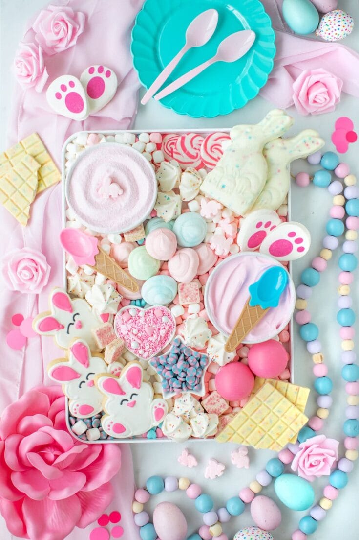 Colorful Easter candy and treats including marshmallow bunnies, lollipops, and chocolates on a pastel pink and blue themed table for spring celebration.