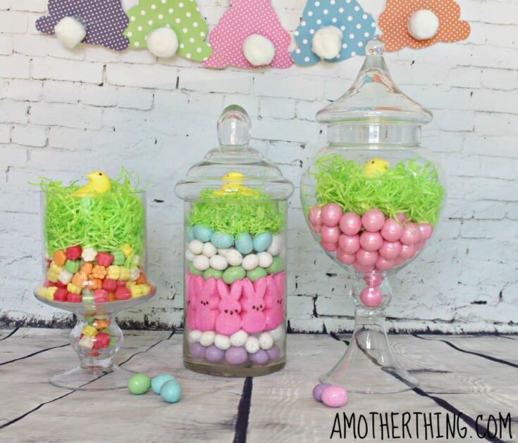 Colorful Easter candy display in glass jars with pink, white, blue, and yellow sweets, decorated with pastel-themed paper clouds and a cheerful spring vibe.