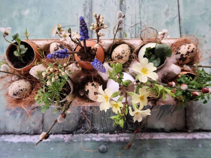 Vase filled with blooming spring flowers, quail eggs, and sprigs of greenery, creating a charming and rustic Easter centerpiece on a weathered wooden surface.