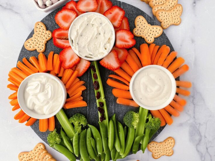 Fresh vegetable platter with carrot sticks, broccoli, and strawberries, served with creamy dipping sauces and animal-shaped crackers, perfect for healthy snacking and family gatherings.