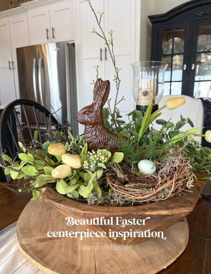 Softly lit Easter centerpiece featuring a rustic wooden bowl with greenery, white tulips, a chocolate bunny, and pastel eggs, perfect for spring decor and holiday celebrations.