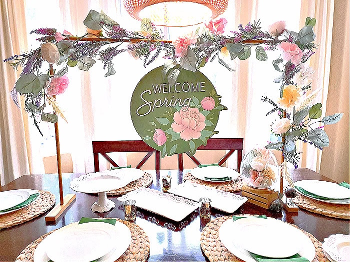 Spring floral table centerpiece with "Welcome Spring" sign, perfect for a festive dining space, featuring fresh flowers, elegant tableware, and seasonal decor for a spring celebration.