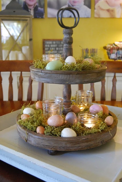 Decorative wooden tiered tray with pastel Easter eggs, moss, and candles for spring or Easter celebrations.